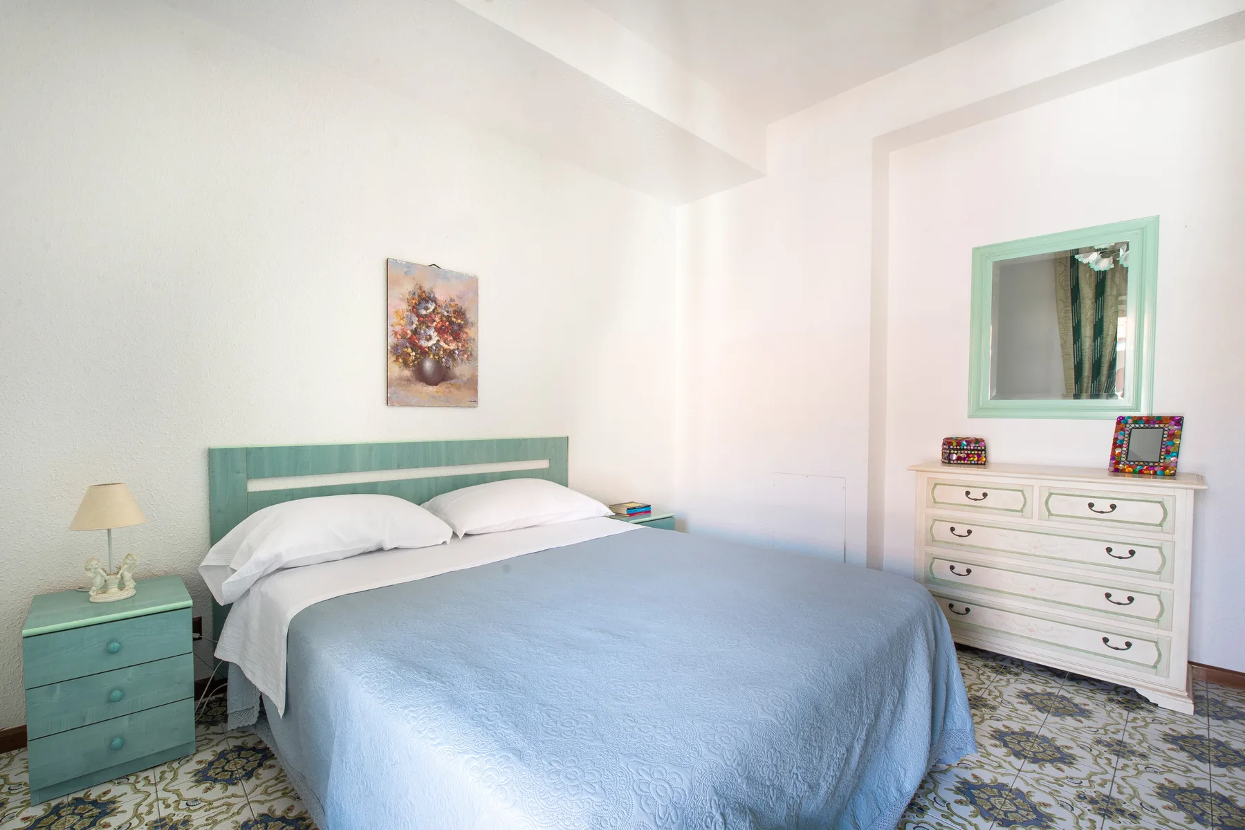 A bright bedroom with a neatly made bed and a dresser beside the window.
