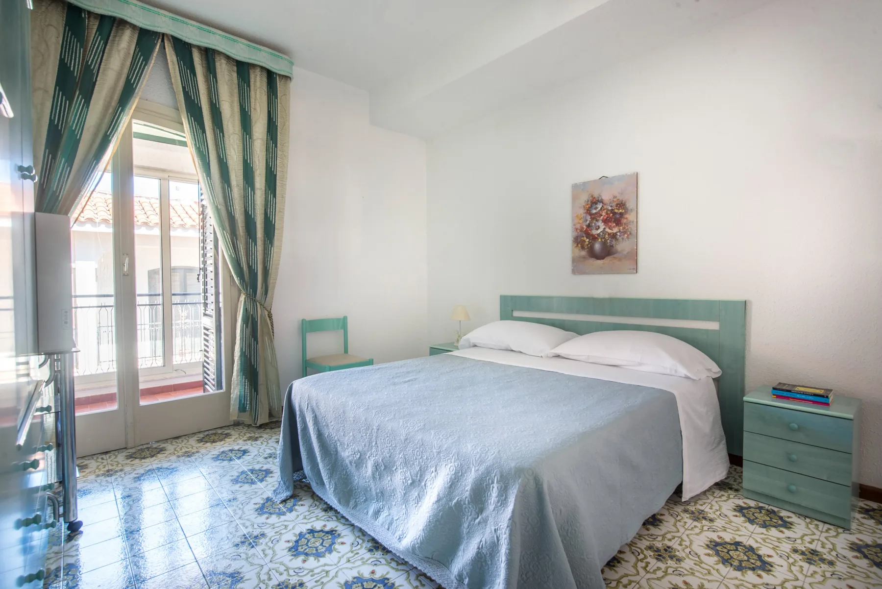 A bedroom with a large bed, green headboard, and tall curtained windows.