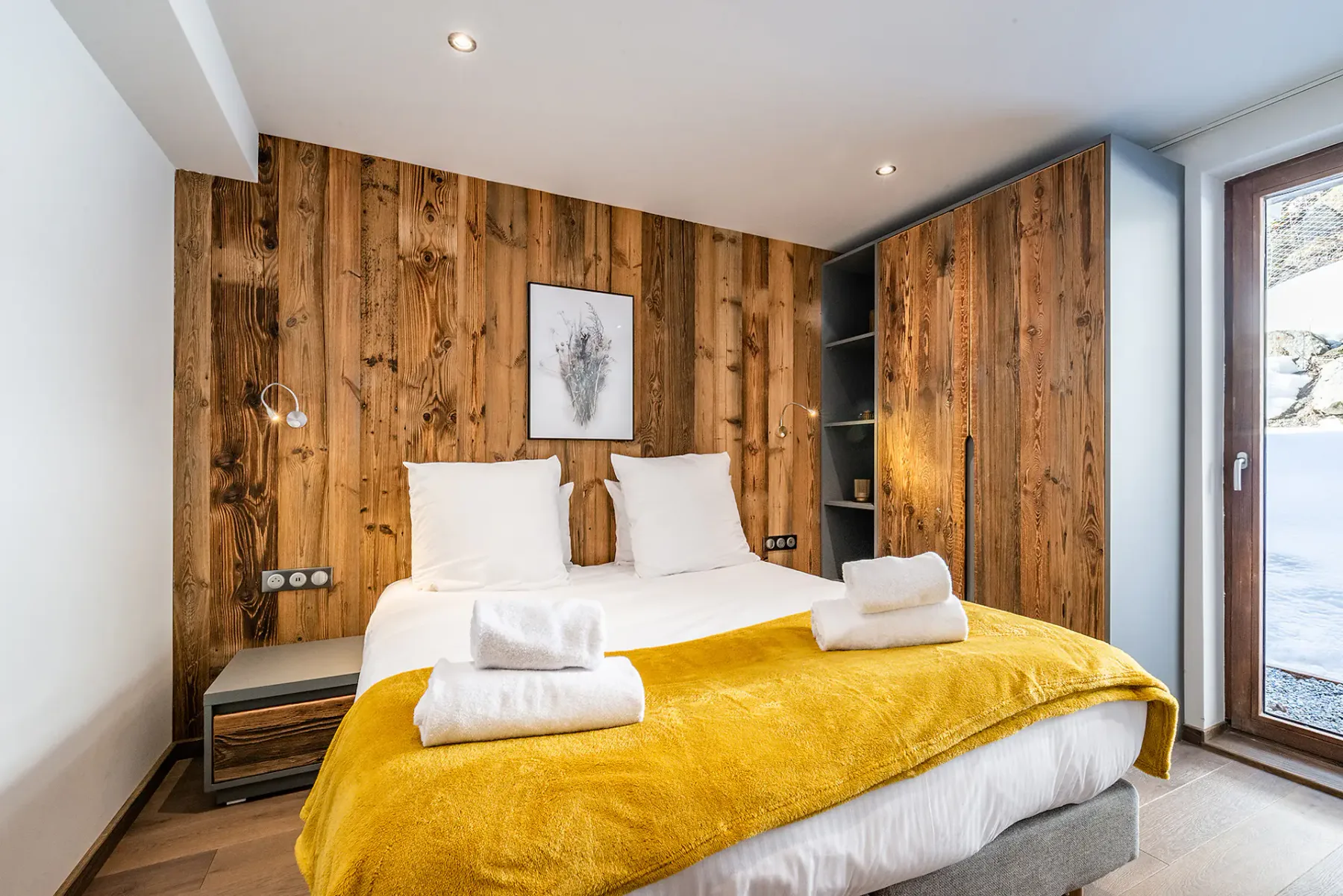 Un dormitorio con una cama doble, almohadas blancas y una manta amarilla mostaza.