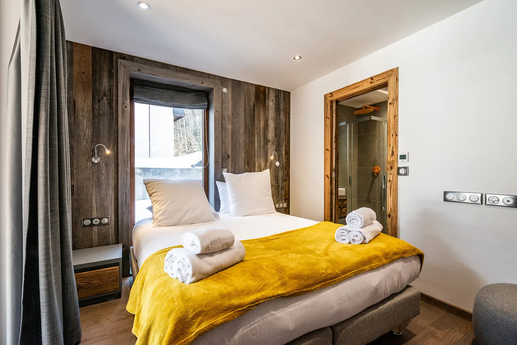 Un dormitorio con una cama vestida con ropa blanca y una manta mostaza.