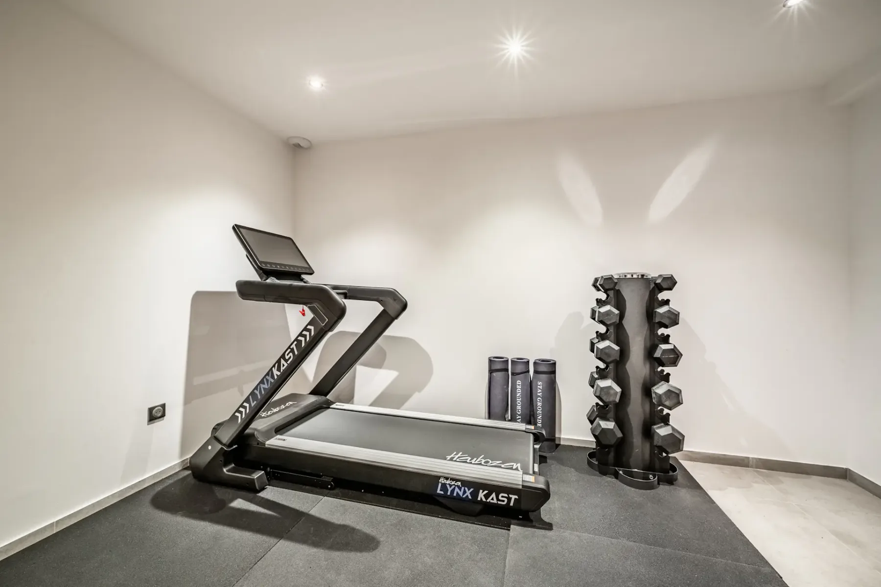 Un pequeño gimnasio con una cinta de correr y un soporte para mancuernas.
