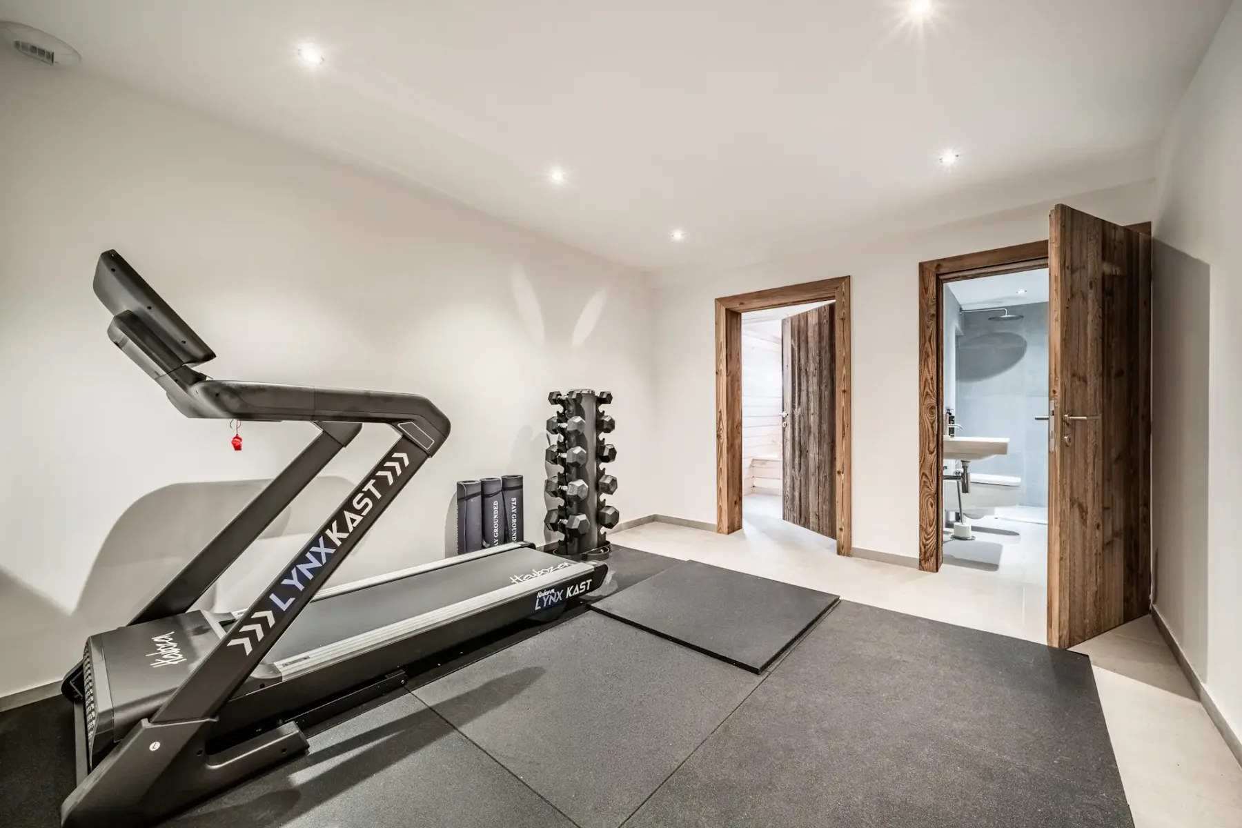 Un gimnasio en casa con una cinta de correr y colchonetas en el suelo.