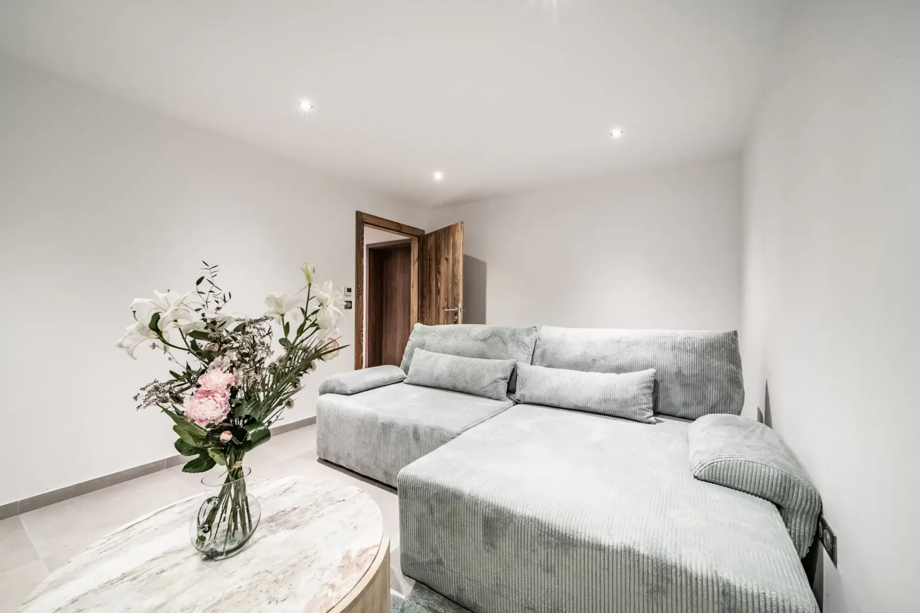 Una sala luminosa con un sofá seccional gris y un jarrón con flores.