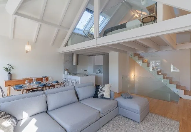 Una luminosa sala de estar con asientos bajo un techo inclinado y grandes ventanas.