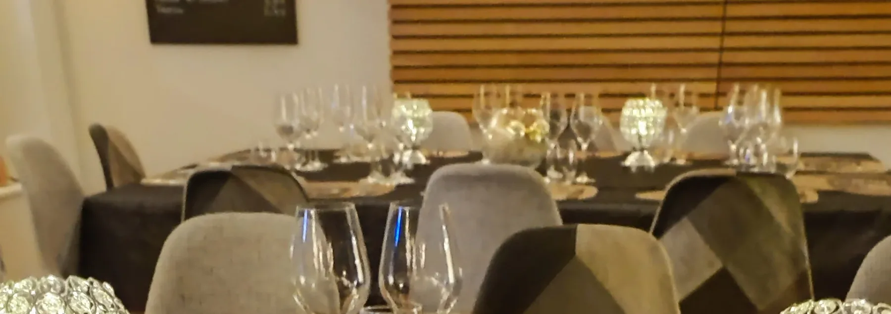Representative hotel space: A dining table is set with glassware in front of wooden blinds.