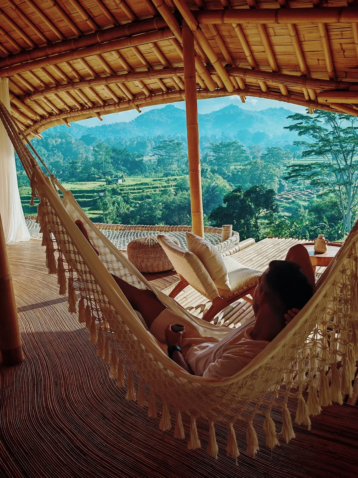A covered outdoor lounging area with hammocks overlooking a green valley.