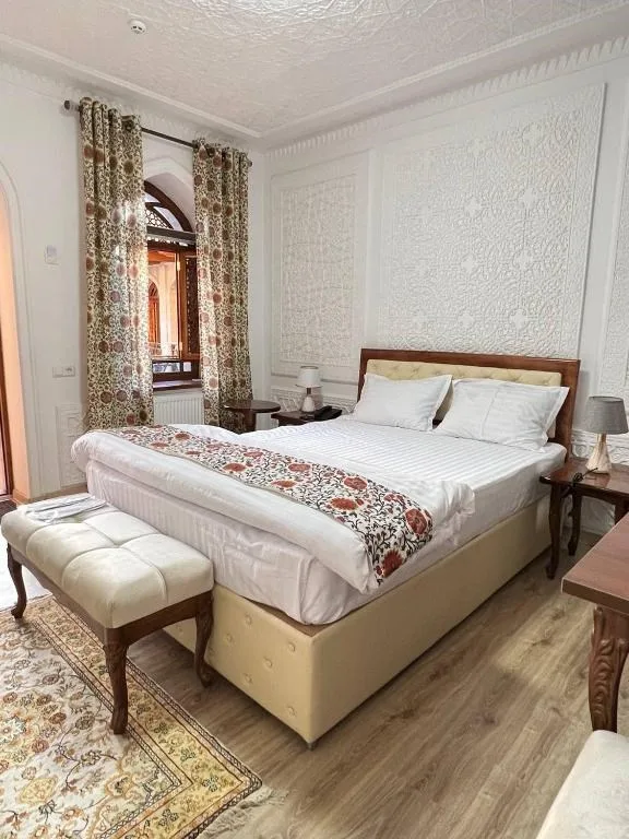Espacio representativo del hotel: Un dormitorio con una cama grande, cortinas estampadas y un banco acolchado.