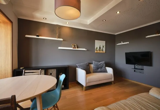 Una sala de estar con un sofá pequeño, un televisor y una mesa de comedor.
