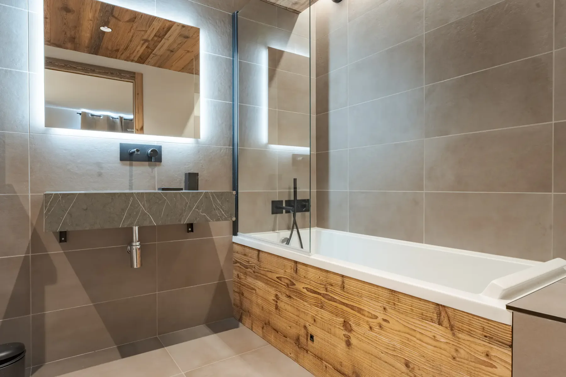 Un baño alicatado con bañera, paneles de madera y un espejo grande.