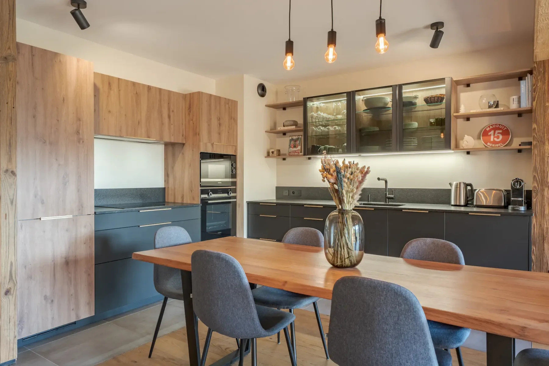 Una cocina moderna y zona de comedor con una mesa de madera y lámparas colgantes.