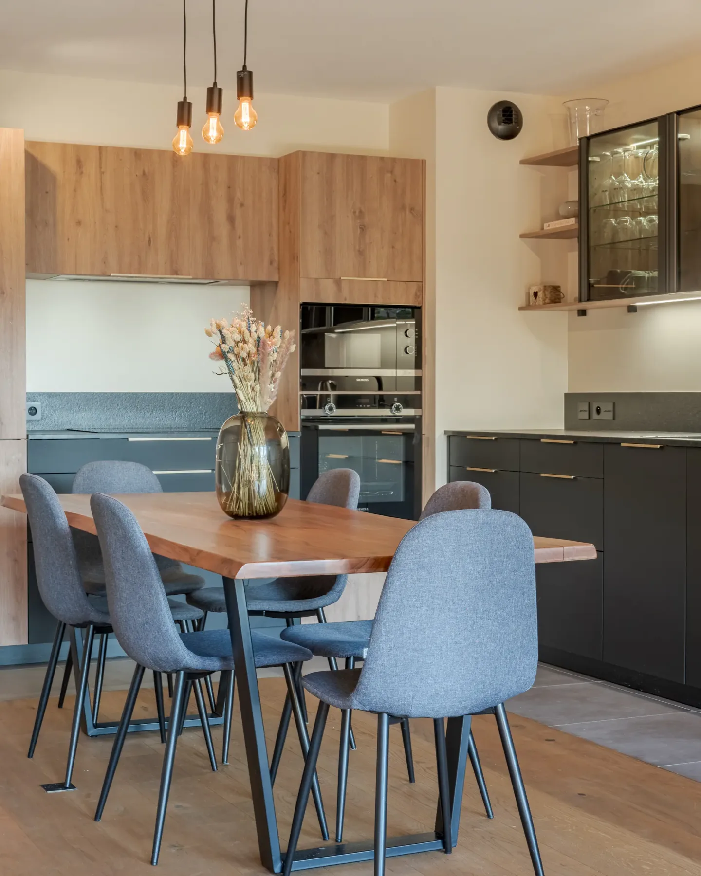Comedor con mesa de madera y sillas tapizadas junto a una cocina moderna.