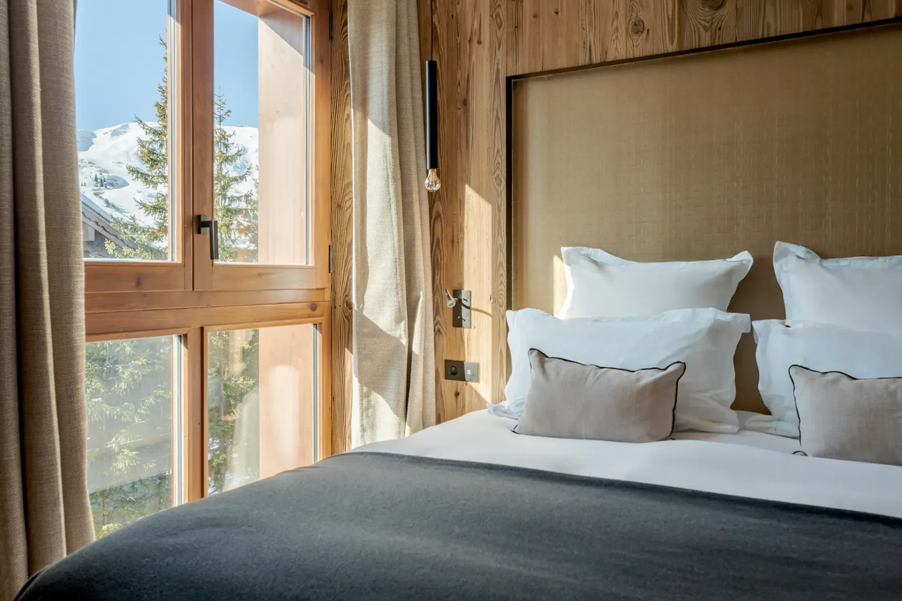 Un dormitorio con una cama bien arreglada junto a una gran ventana con marco de madera.