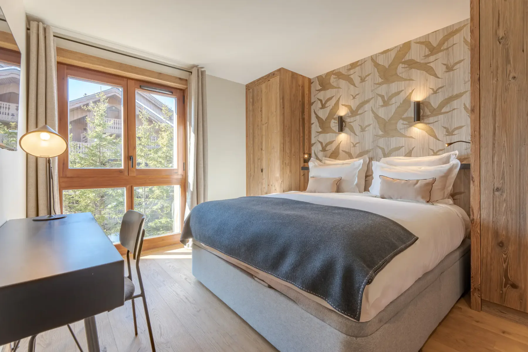 Un dormitorio con una cama bien hecha y grandes ventanas con vistas a la vegetación.