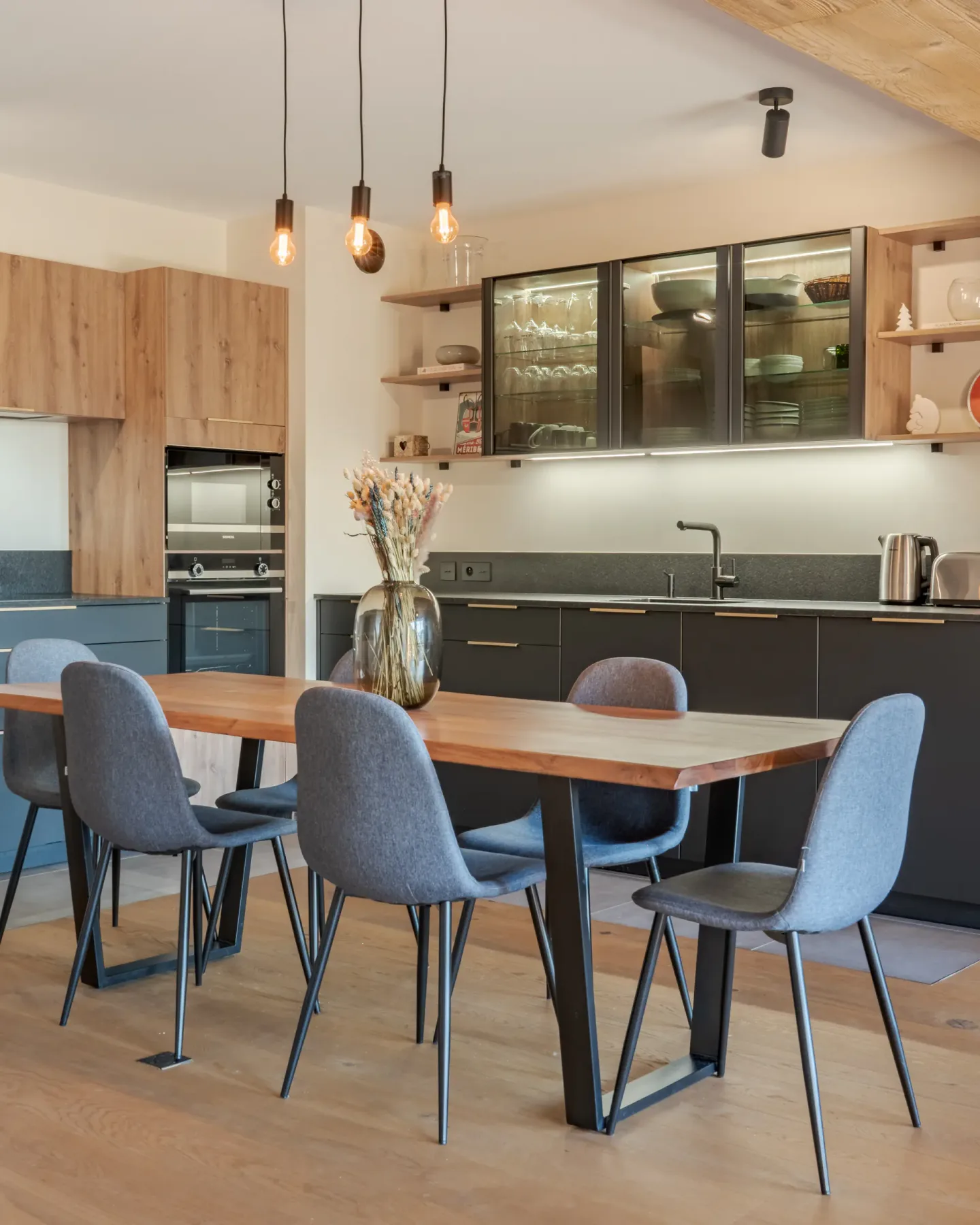 Una mesa de comedor con asientos tapizados está frente a una cocina moderna.