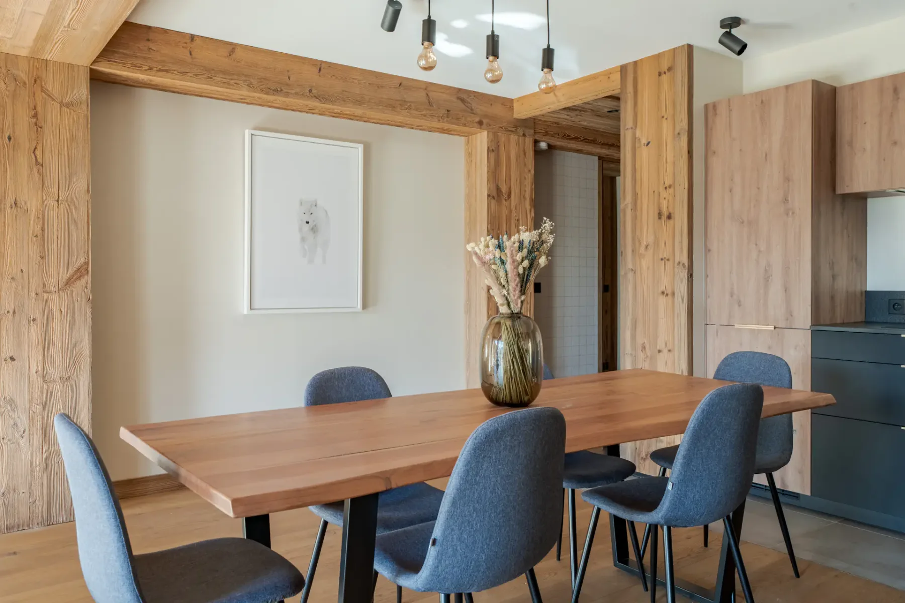 Comedor con una mesa de madera, asientos azules y un jarrón con flores.