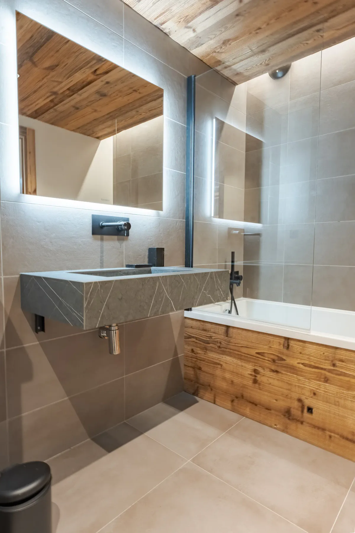 Un baño alicatado con una bañera revestida de madera y un lavabo suspendido.