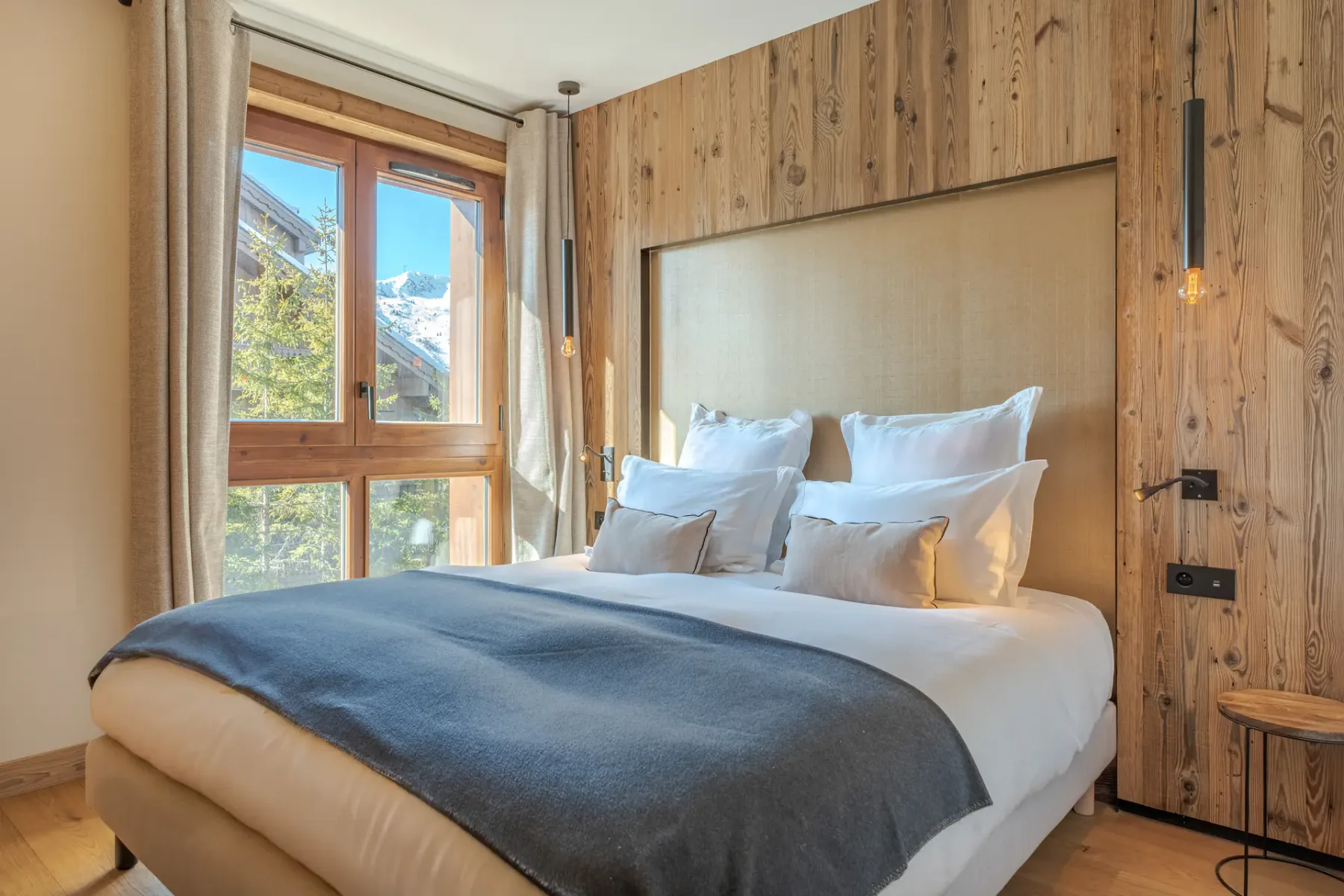 Un dormitorio con una cama bien tendida y grandes ventanas con vistas a árboles y montañas.