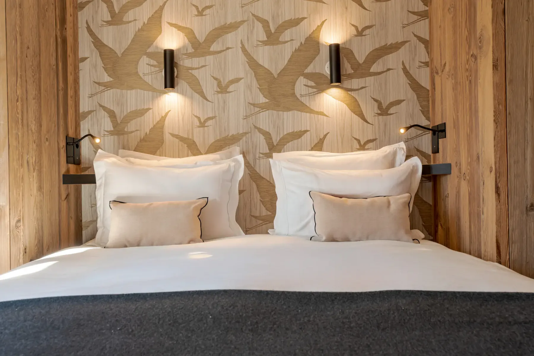 Un dormitorio con una cama bien tendida y papel tapiz con motivos de aves.