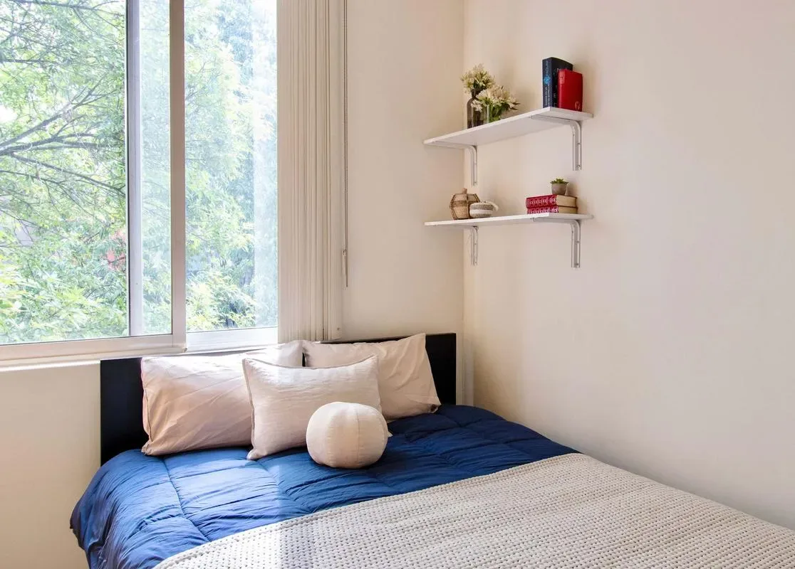 A bedroom with a bed covered in blue bedding beside a large window.