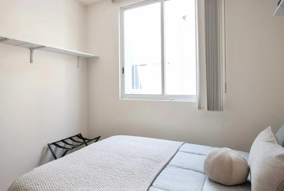 A bedroom with a bed beneath a window and a small wall shelf.