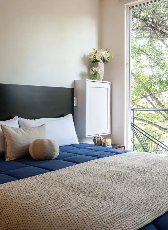 A bedroom with a blue bed and a large window overlooking leafy trees.