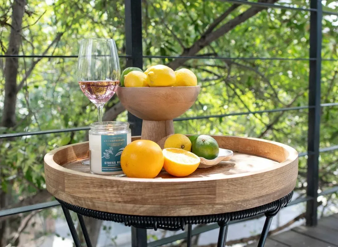A small round table holds a bowl of citrus fruit and a glass beside a leafy view.