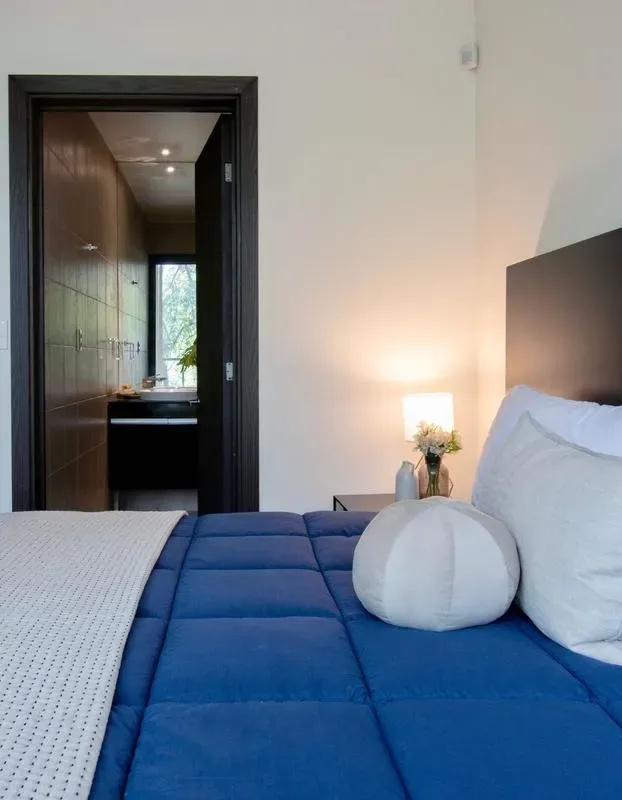 A bedroom with blue bedding and an open doorway to a bathroom.