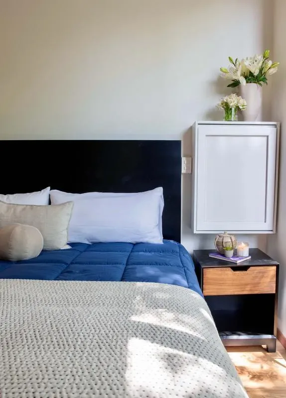 A bedroom with a bed dressed in blue bedding and a bedside table.