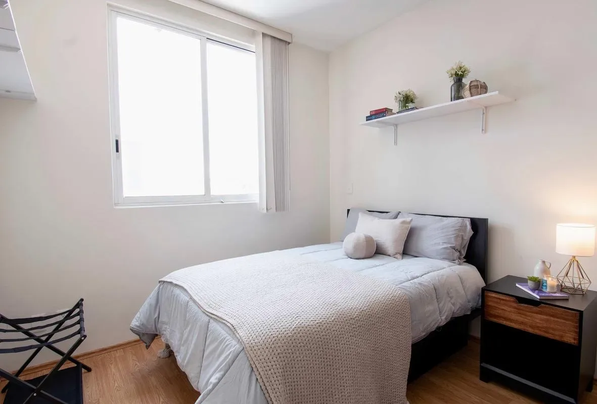 A bright bedroom with a neatly made bed and a large window.
