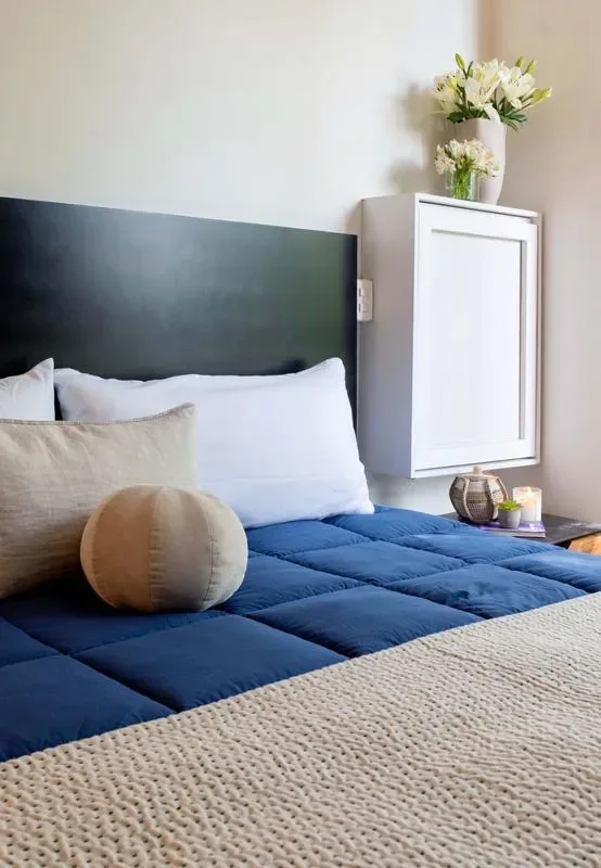 A bedroom with a bed dressed in a blue quilt and light pillows.