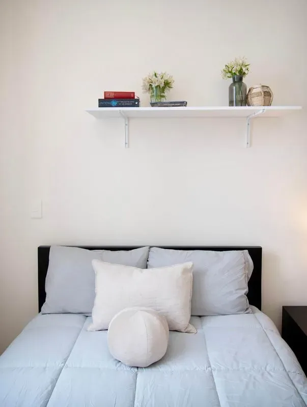 A bedroom with a neatly made bed and a floating shelf above it.