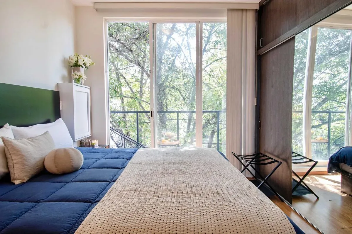 A bedroom with a bed beside floor-to-ceiling windows overlooking trees.