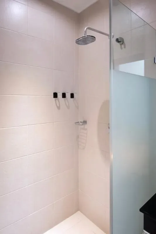 A tiled shower with a glass partition and overhead showerhead.