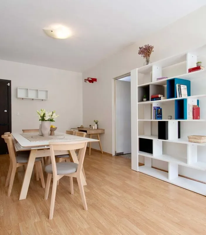 A bright dining area with a table and chairs beside a white shelving unit.