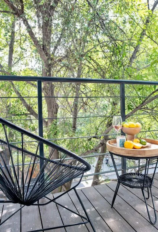 A balcony seating area overlooks leafy trees, with a small table holding fruit.