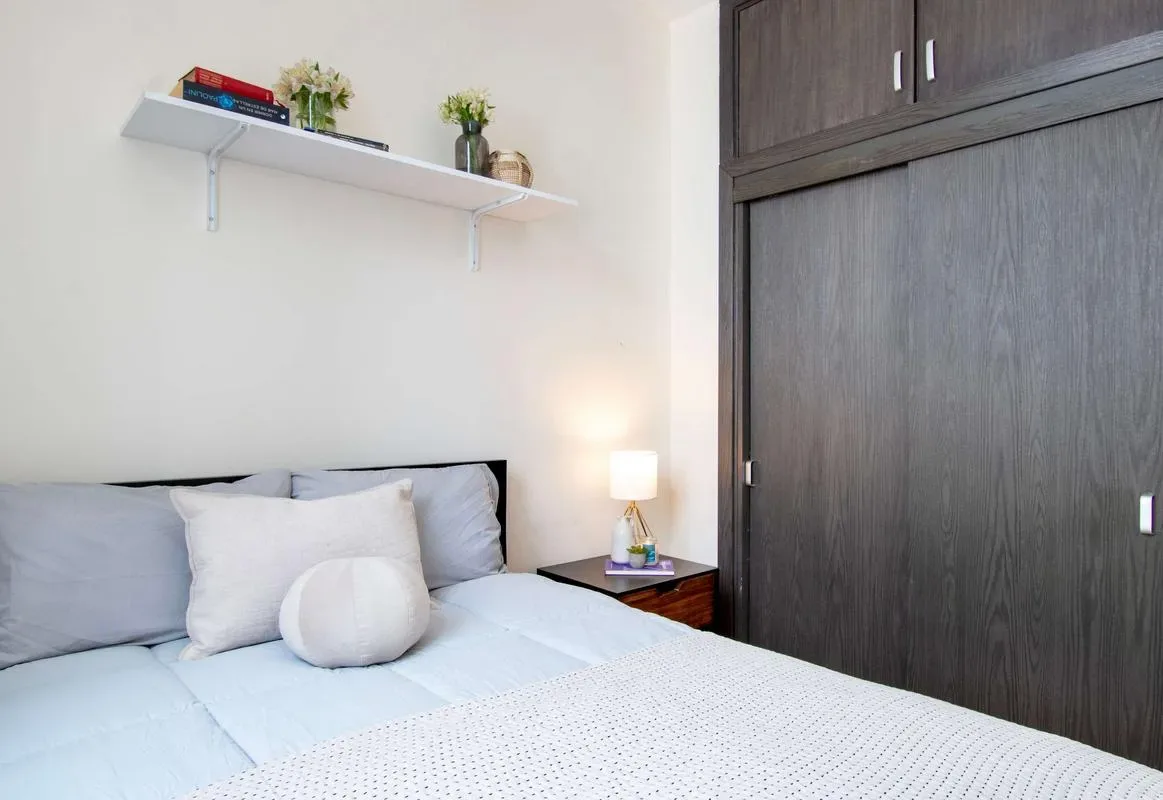 A bedroom with a bed, pale bedding, and a dark built-in wardrobe.