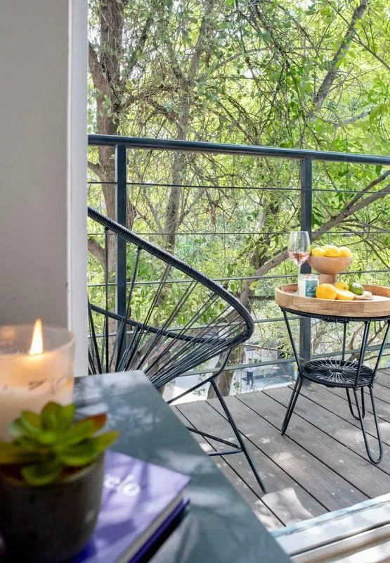 A balcony seating area overlooks leafy trees, with fruit on a small table.