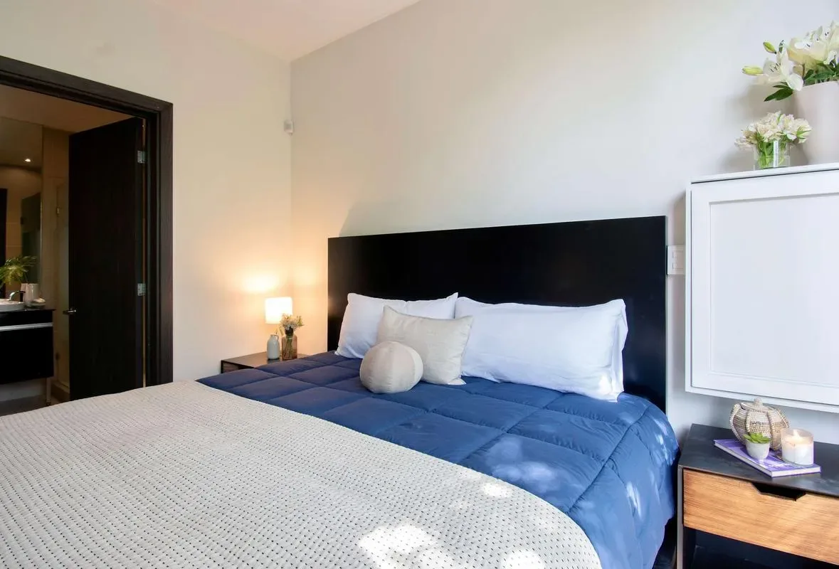 A bedroom with a blue bed, white pillows, and a bedside lamp.