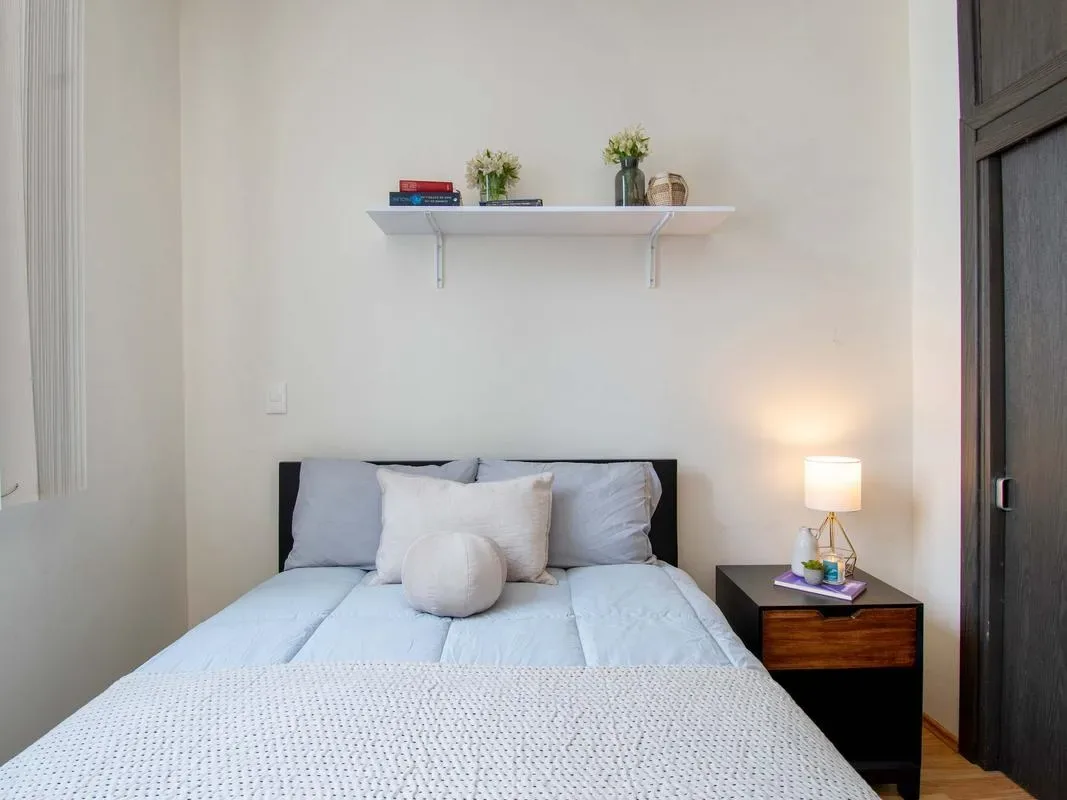 A bedroom with a neatly made bed and a shelf above the headboard.