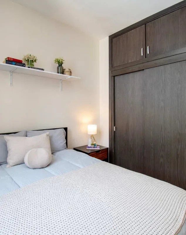 A bedroom with a neatly made bed, bedside table, and dark built-in storage.