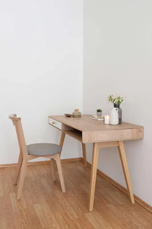 A wooden desk and chair sit in a bright room with a few small decorations.