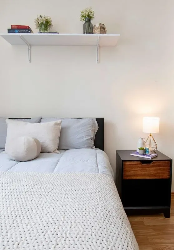 A bedroom with a neatly made bed and a bedside table with a lamp.
