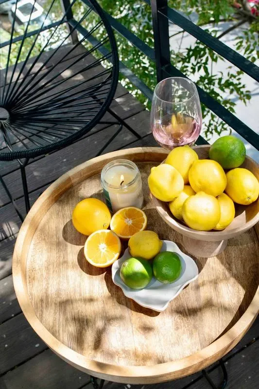 A round outdoor table holds citrus fruit, a candle, and a glass beside a patio chair.