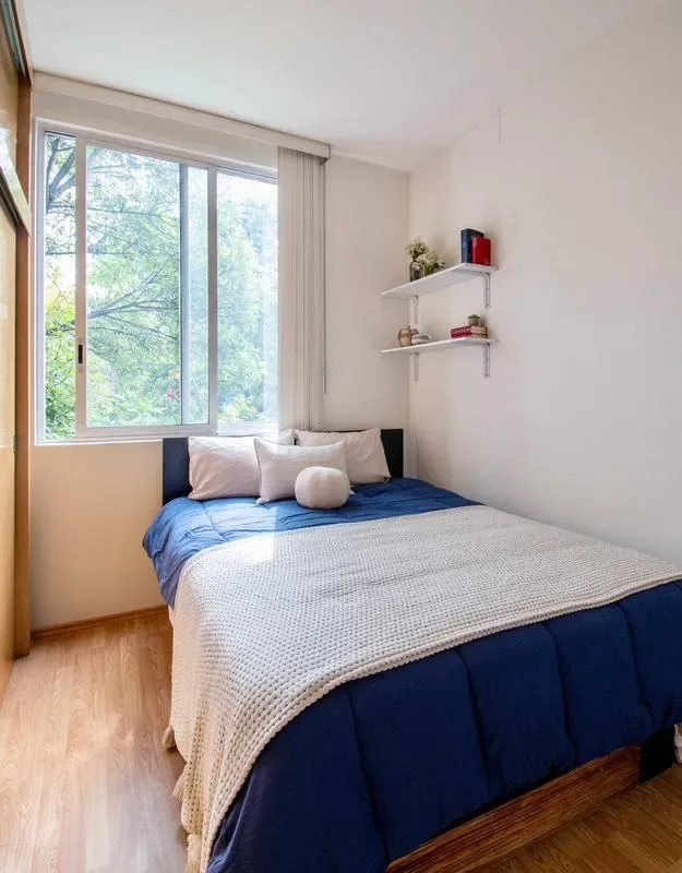 A bedroom with a bed dressed in blue and white bedding beside a large window.