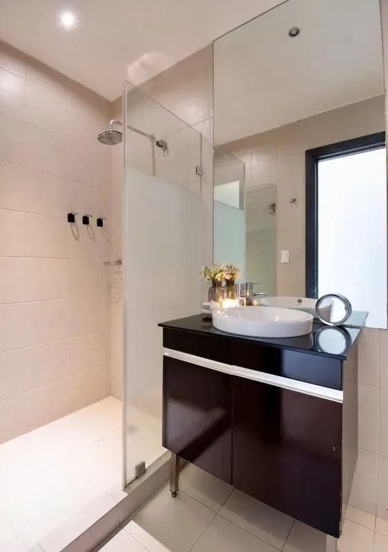 A bright bathroom with a glass shower and a dark vanity topped by a white sink.