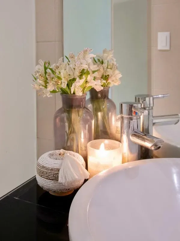 A bathroom vanity displays flowers and a lit candle beside the sink.