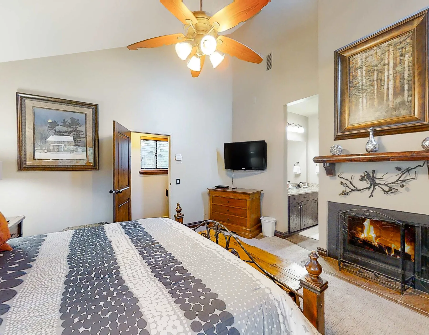 Dormitorio con ropa de cama estampada, un televisor y una chimenea.