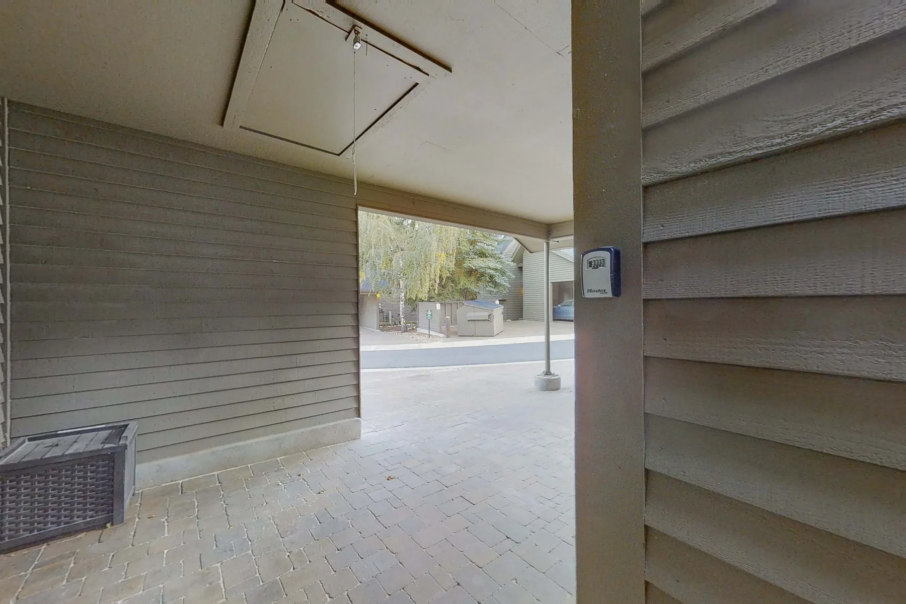Zona común: Un pasillo exterior cubierto da a una zona pavimentada con árboles al fondo.