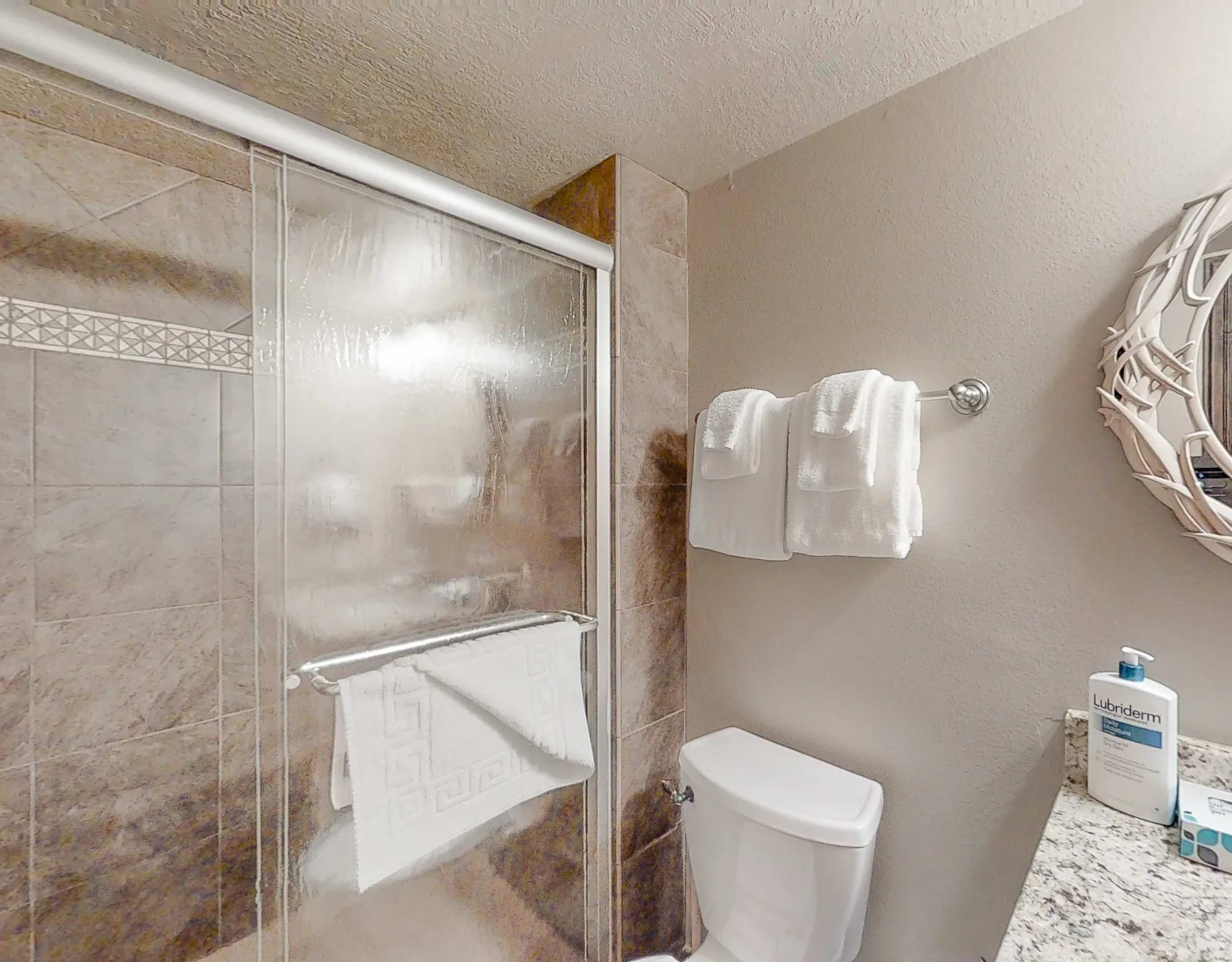 Un baño alicatado con ducha de vidrio, inodoro y toallas colgadas en la pared.