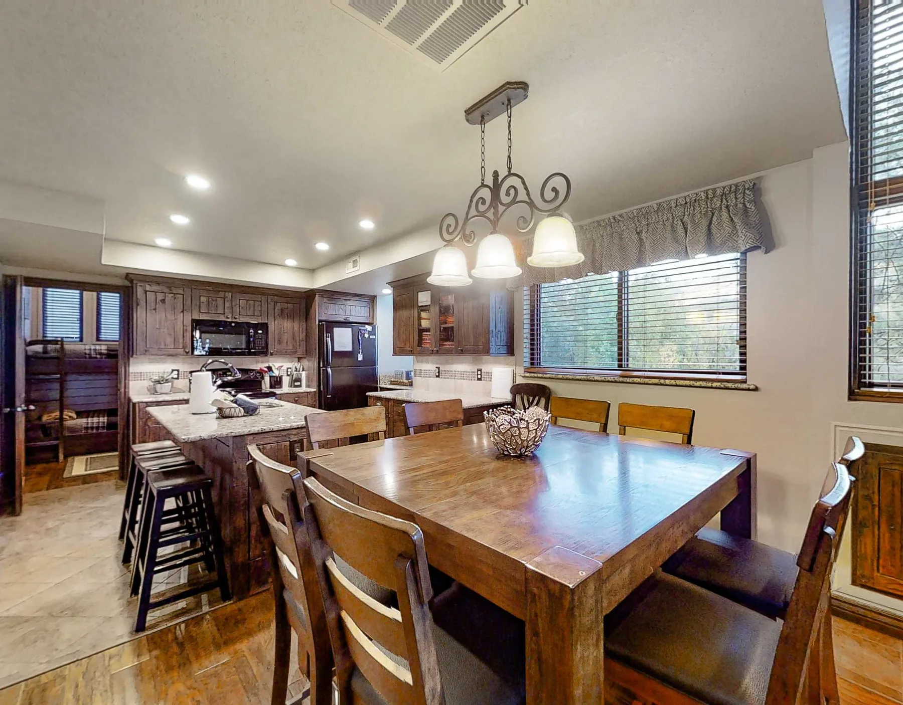Cocina y comedor con una gran mesa de madera bajo lámparas colgantes.